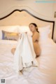 A woman sitting on a bed covered in a white sheet.