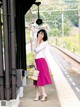 A woman standing on a train platform with a basket bag.