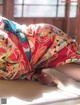 A woman laying on a bed covered in a colorful kimono.