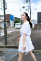 A woman in a white dress is walking down the street.